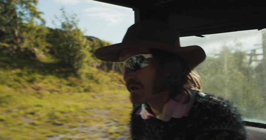 A man wearing a hat and sunglasses drives a utility vehicle in midday
