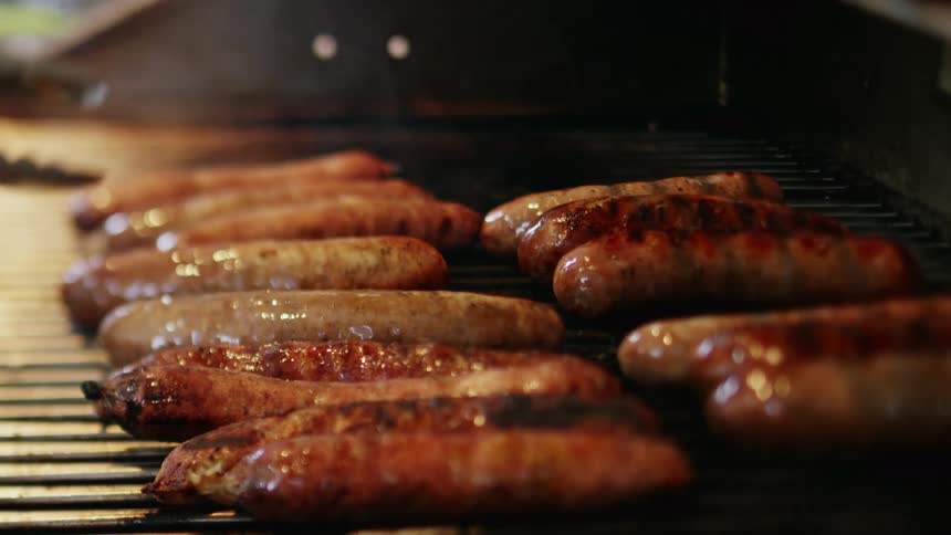 A person is flipping sausages on the grill