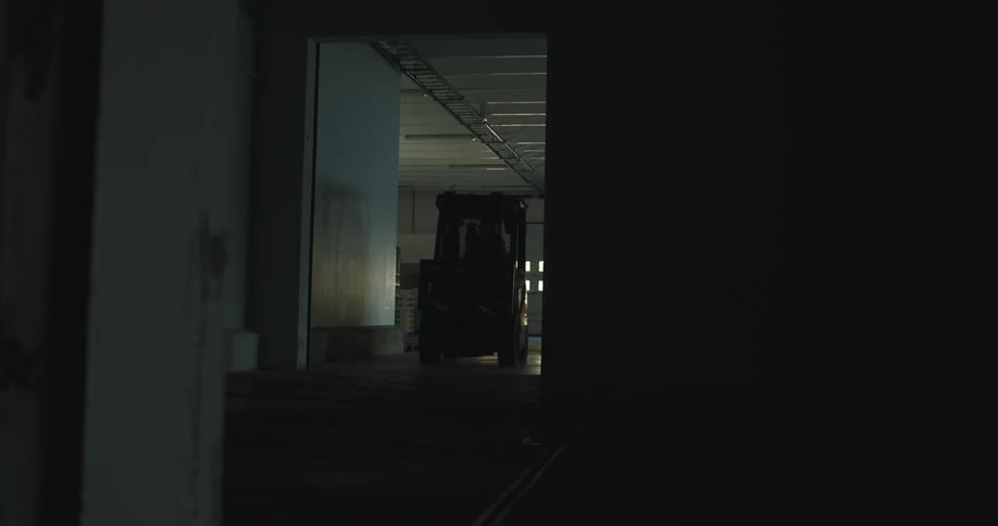 A warehouse with a forklift driver moving around and parking in the dark