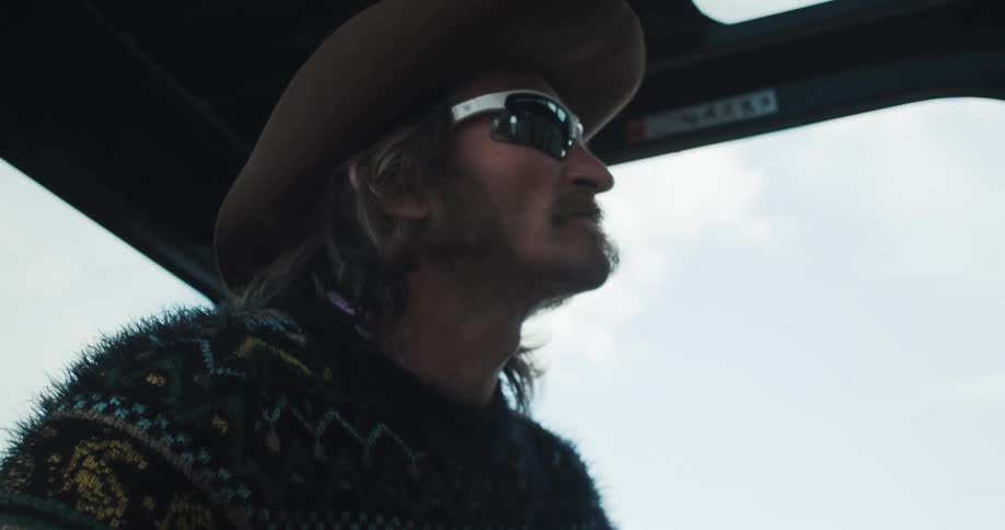 A man wearing a hat and sunglasses looking focused while driving a vehicle