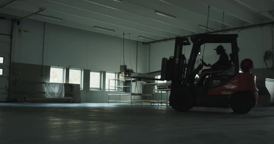 Forklift operator moves vehicle across room before parking it and exiting to sit on the platform
