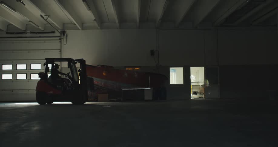 Forklift operator drives forklift through large empty room in warehouse
