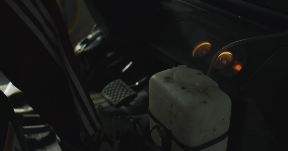 Man pilots vehicle with gauges and white liquid container near foot pedals