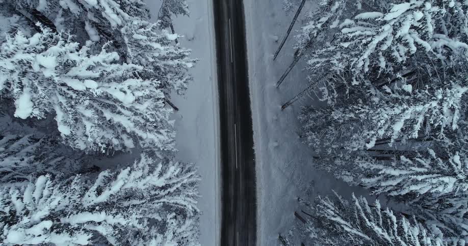 Aerial view of zooming out over a road passing through a heavily forested area covered in snow