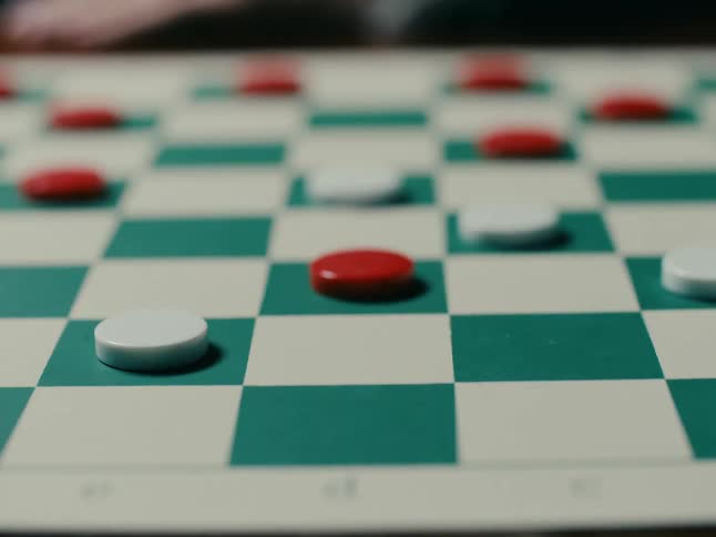 A player in a checker game reaches their hand out and moves a white game piece to a green square