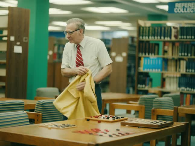 Man standing near library table with checker boards removes jacket and walks away