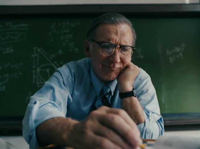 Math teacher sitting in classroom alternating playing solo checkers and grading papers
