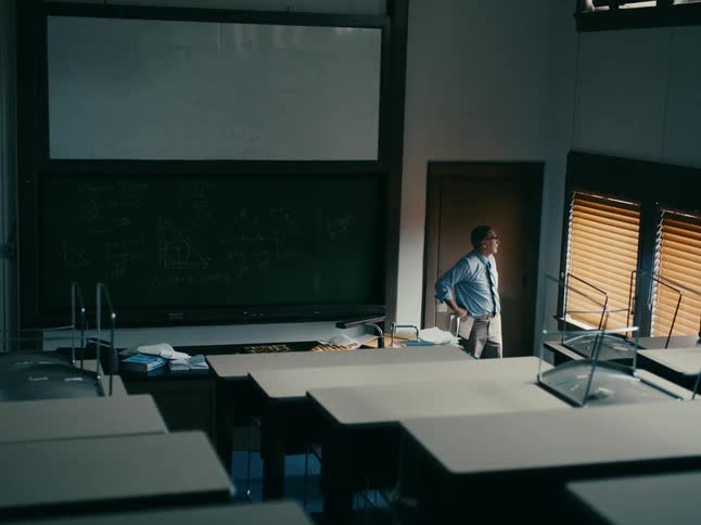 A teacher is standing in an empty classroom