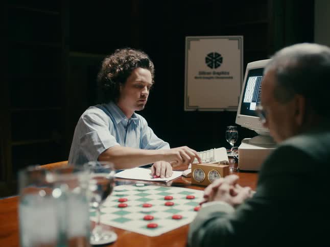 A man typing on the keyboard playing and inputting chess data in his computer and playing chess with another man