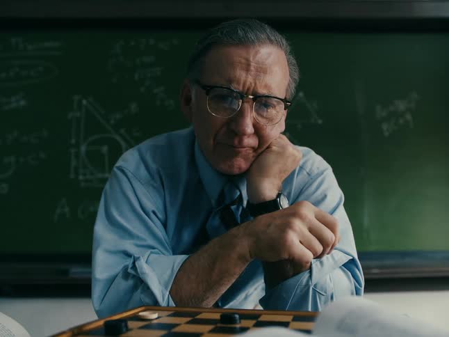 A man plays chess while sitting in front of the chalkboard in his classroom