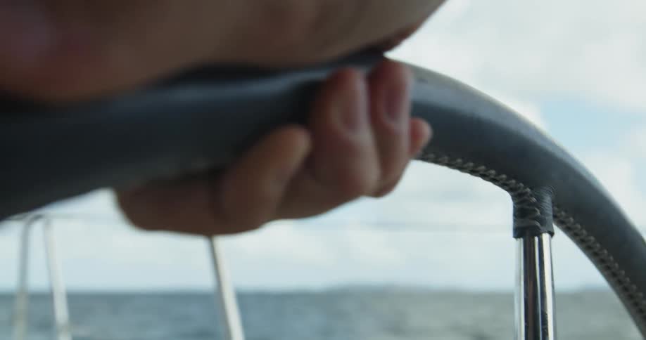 An up close of a persons hand on a boat wheel