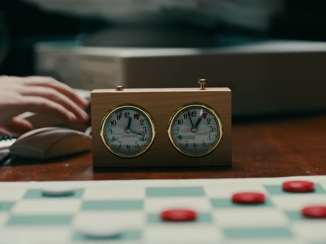 Close up of a chess clock in front of a checkers board being used by two players