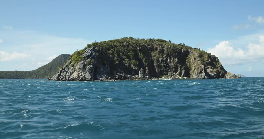 Footage of an island in the middle of the blue ocean waters at daytime seen from a boat