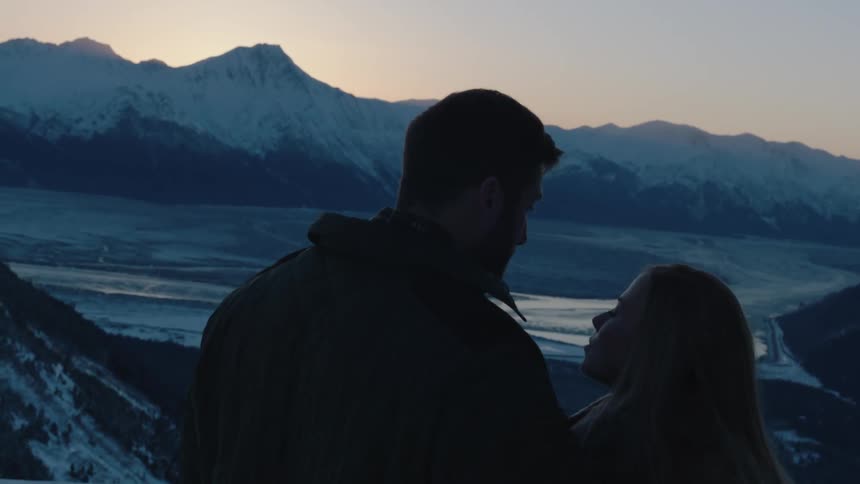 A man and woman stare into each others eyes and then turn toward a view of some mountains