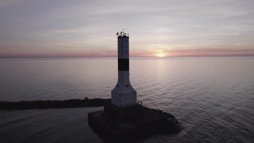 A tower stands tall near the break wall as ripples in the water are reflected by the sun setting on the horizon