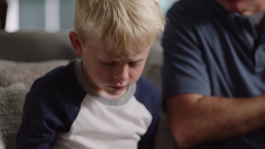 A man opens a binder with cards in it to show his grandson sitting next to him