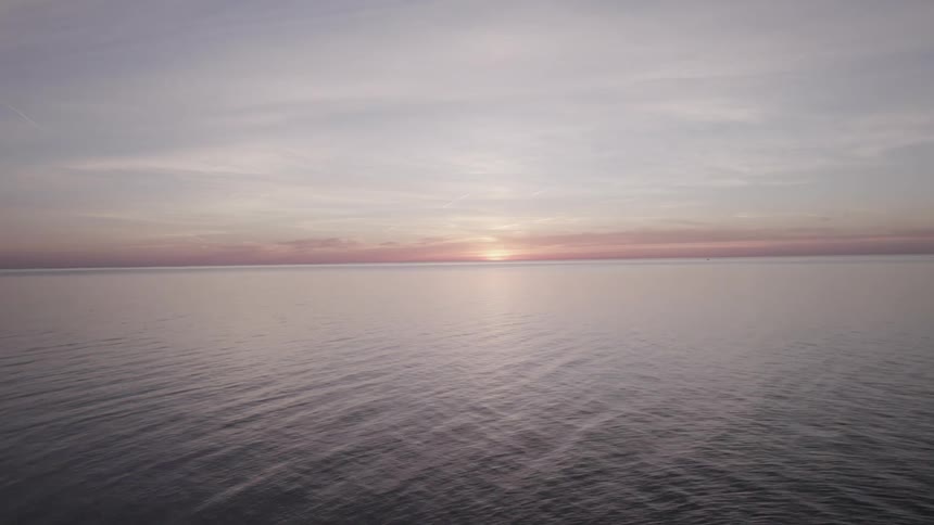 Aerial view moving across water at sunset past jetty and lighthouse