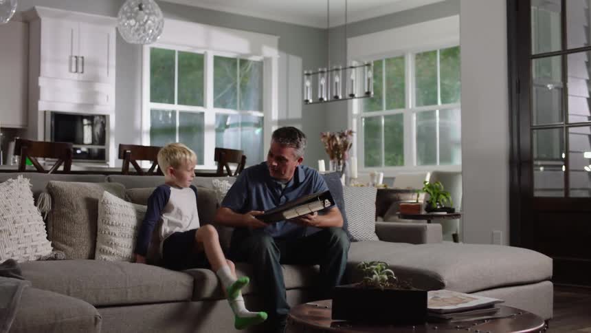 A man shows a board game to his son while sitting on the couch at home
