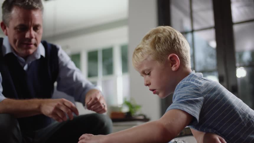 Father and son sitting on the floor in the living room assembling a puzzle