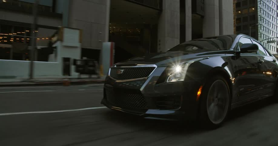 Luxury black car drives with headlights on on the city streets at daytime