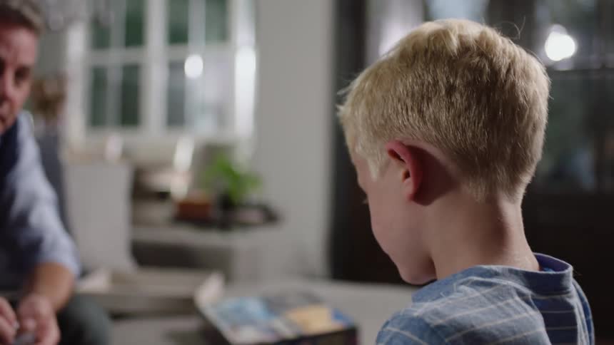 A boy plays a board game with his father at home