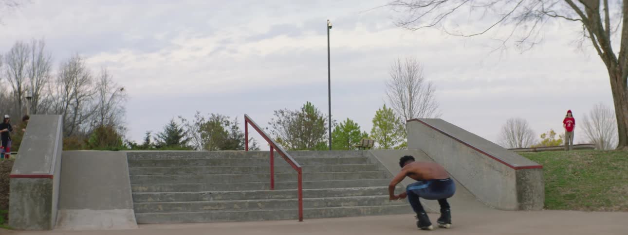 Young muscular shirtless man wearing roller skates jumps down a row of stairs on a park