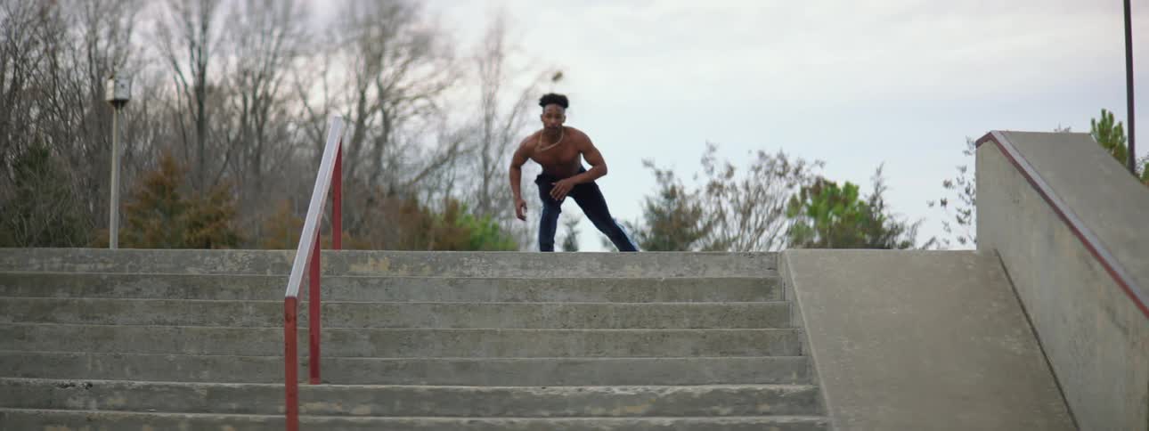 Young muscular shirtless man wearing roller skates jumps down stairs on a park