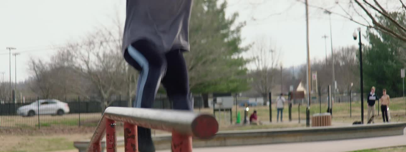 Young muscular shirtless man wearing roller skates slides up a railing in a park