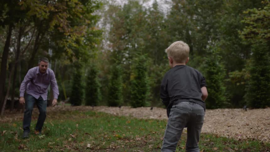 Father and son play football on the back yard close to a forest at morning