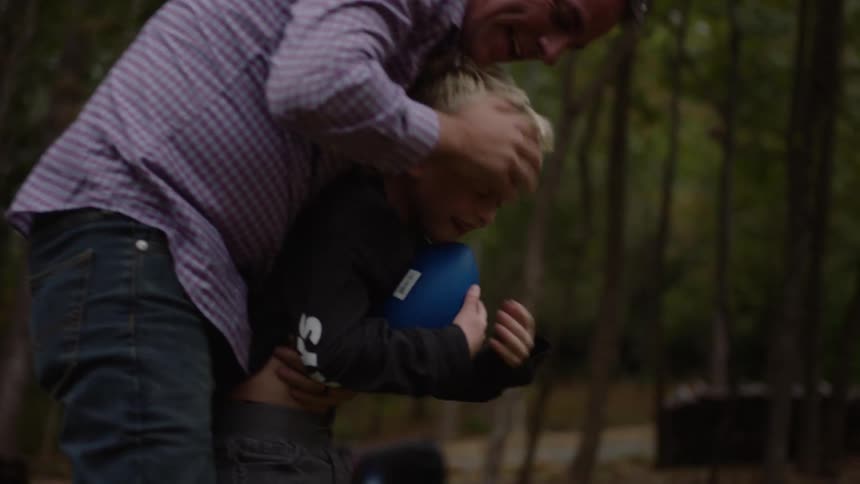 A grandfather plays with his grandson outside with a ball