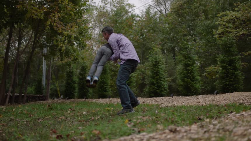 Father and son playing football outdoors on grassy area near trees