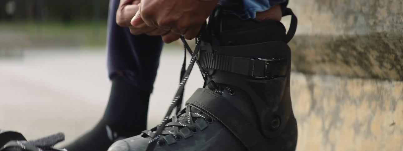Tying laces on rollerblades while sitting on cement block outdoors