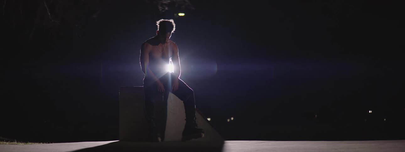 Man sits on concrete block at night as vehicles pass on road in the background
