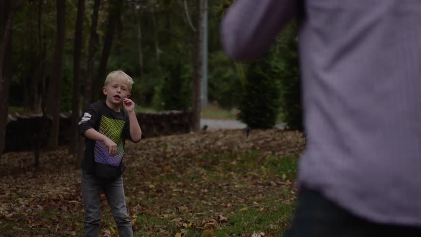 Father and son toss blue football back and forth in fallen leave strewn yard