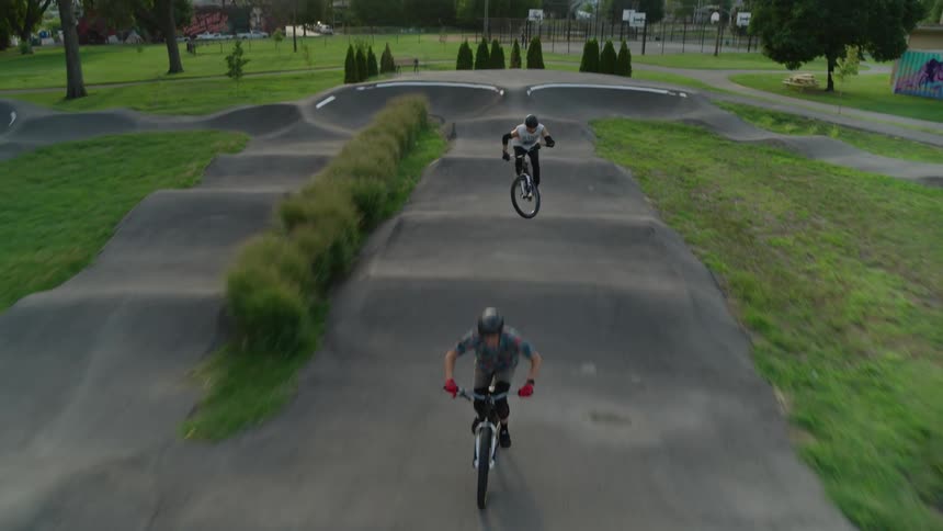 Two cyclists ride over bicycle course at park with skyline in the background