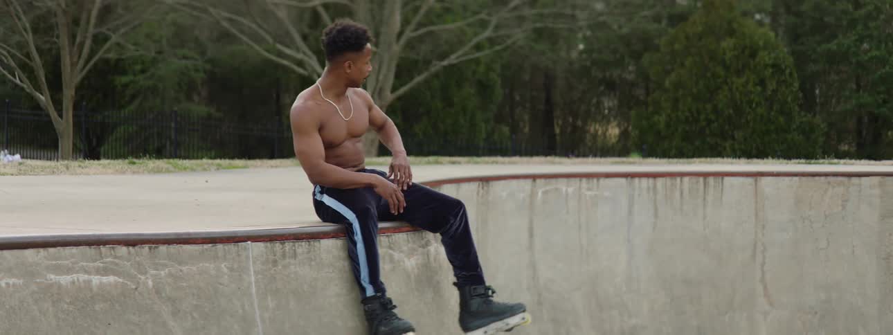 A man on roller skates rolls to the edge of a ramp and sits down on the concrete