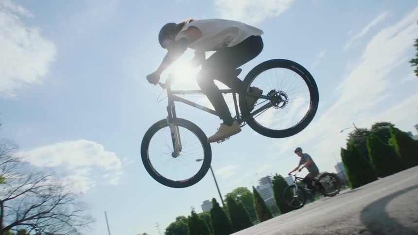 Teenager on bicycle in park doing jumps on pavement