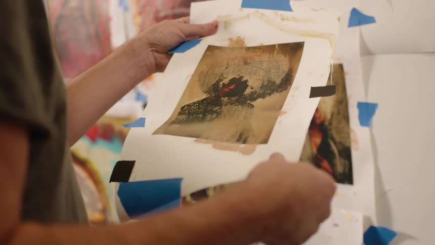 A mans arms and hands are shown holding a piece of paper with abstract art on it