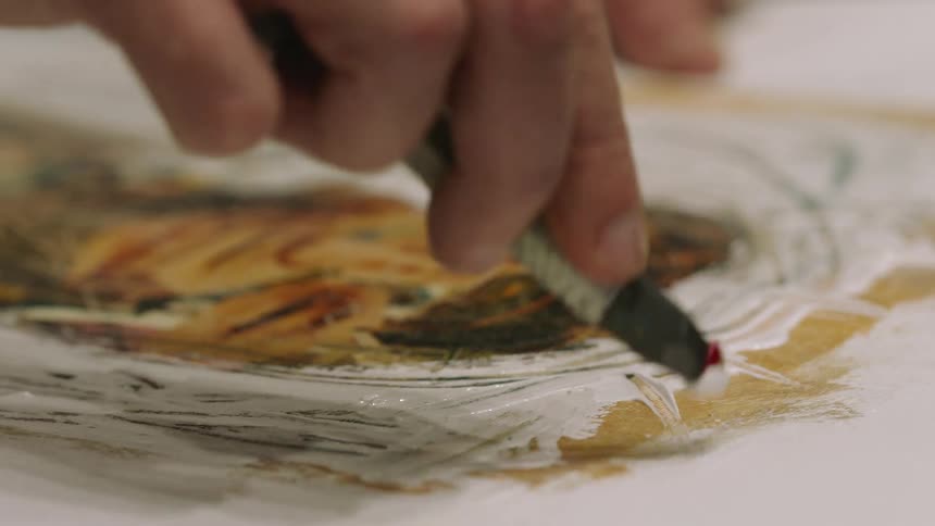 A mans hand is shown applying paint to a painting with a brush
