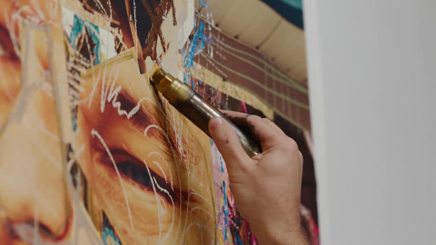 A man uses a gold marker to draw onto a painting