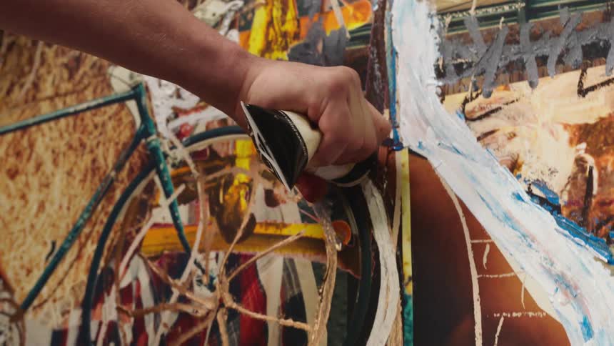 Artist applies paint to artwork attached to wall using tube of paint