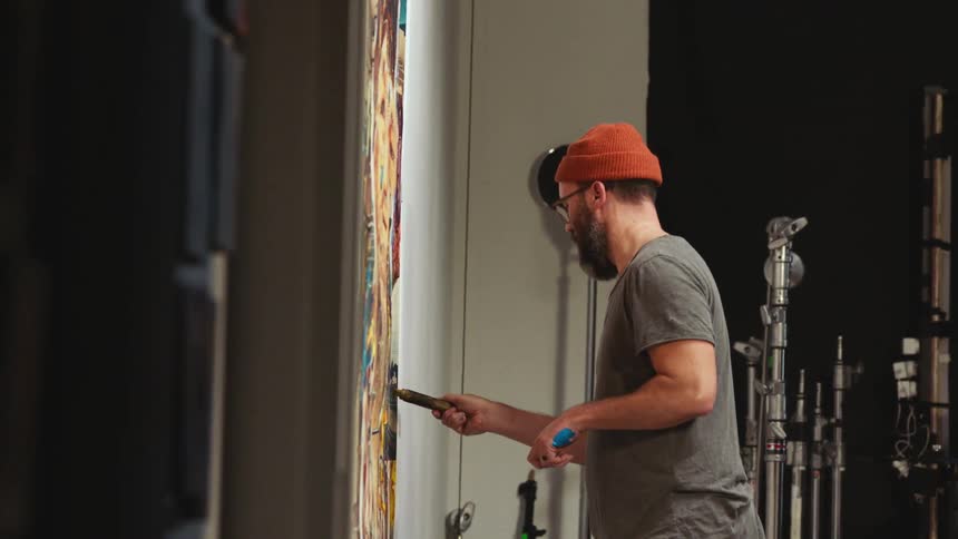 Man stands painting on panel hanging on wall in studio