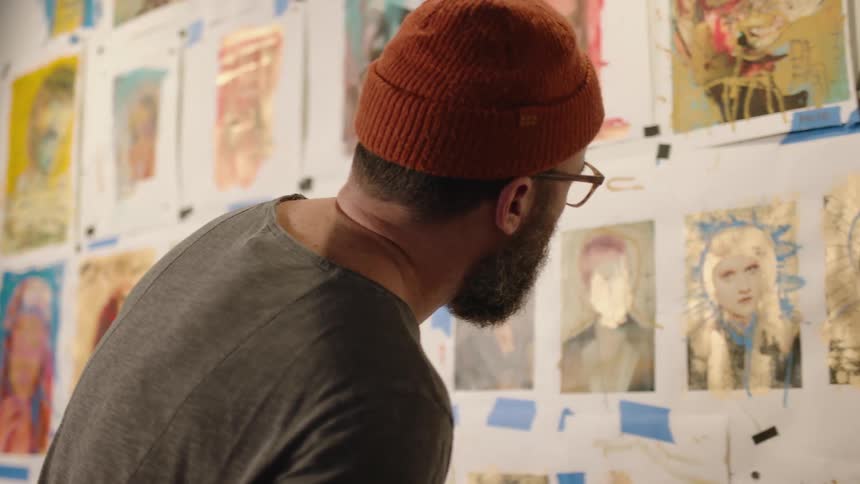 Close up of an artist inspecting the paintings displayed on a wall