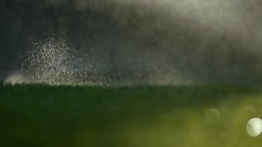 Sprinkler system spraying water over green grass on a field at night