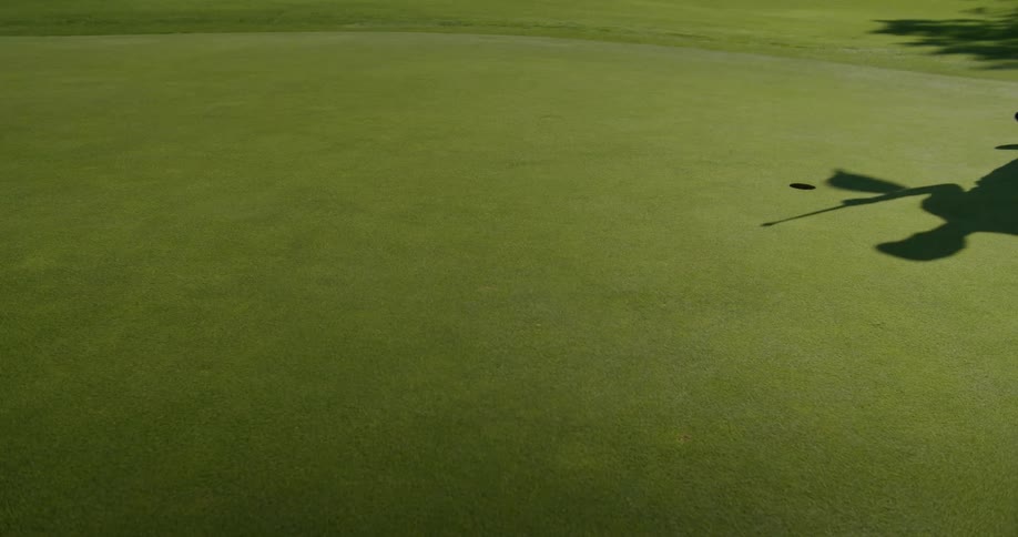 Shadow of a golfer removing a flag from a hole on a golf course