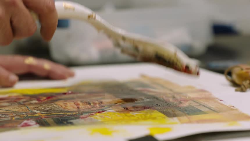 Close up of an artist using a large spatula to brush over an oil painting