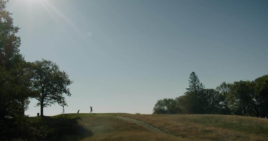 Golfer on top of hill onsunny day takes a swing
