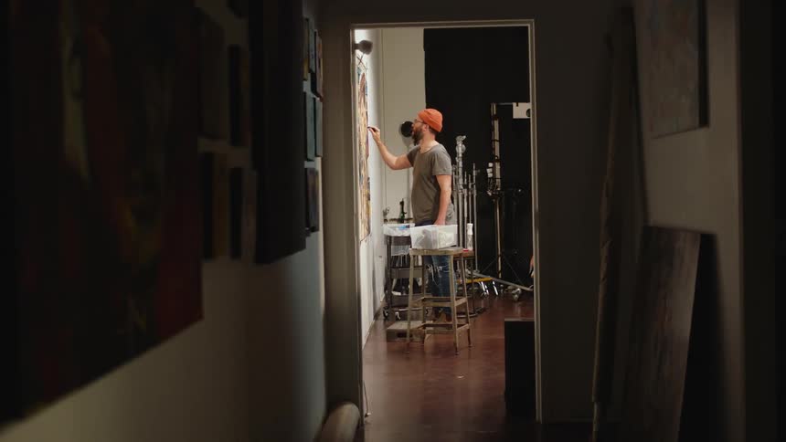 An artist in an apartment is painting on a large canvas while standing