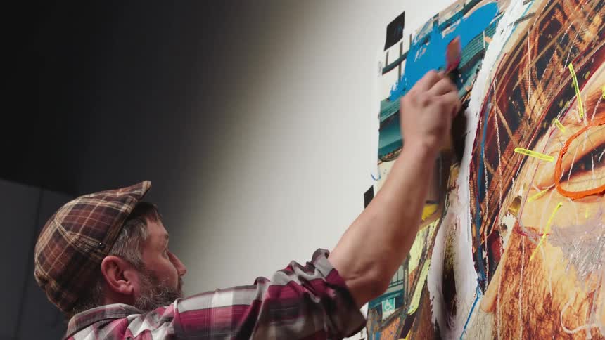 Man with beard tweed cap and plaid shirt paints portrait of man in oils