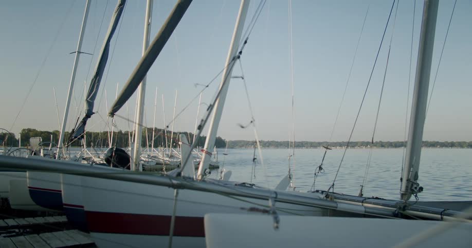 Sailboats with their sails wrapped up or removed are lined up at the docks as the wind blows over the water on the lake behind them